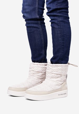 Vita kviltade anklarstövlar med en slät beige sula, som har en subtil logotyp och texturerad mönster. I kombination med åtsittande blå denimjeans.