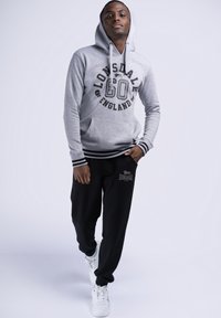 Felpa grigia con scritte e logo neri, abbinata a pantaloni jogger neri con un piccolo logo. Sneakers bianche completano l'outfit.