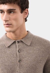 Brązowa dzianinowa koszulka polo o teksturowanym wykończeniu, z kołnierzykiem i trzema guzikami. Materiał wydaje się miękki i średniej wagi.