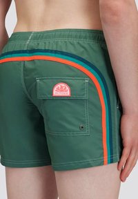 Groene zwemshorts met een patchzak, voorzien van oranje en blauwe gestreepte accenten. Gemaakt van lichtgewicht materiaal met contrasterende stiksels.