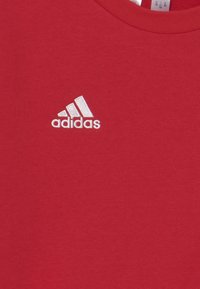 Felpa rossa in cotone con logo Adidas ricamato di colore bianco sul lato sinistro del petto. Collo rotondo semplice e texture liscia.