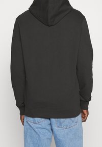Sweatshirt à capuche noire avec une texture lisse, des poignets et un ourlet côtelés, et une coupe décontractée, associé à un jean en denim bleu clair.