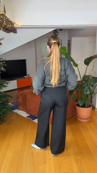 Γκρι φαρδιά φούτερ με μαύρα γράμματα, συνδυασμένο με μαύρο παντελόνι φαρδύ και ασημί αθλητικά παπούτσια, σε περιβάλλον σαλονιού.