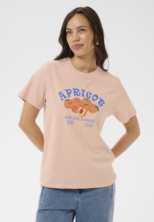 Frau trägt ein helles Pfirsich-T-Shirt mit einer Aprikosen-Grafik und den Schriftzügen "APRILOT", "ENDLESS SUMMER", "SOUTHERN BEACHES" und "LIVE IN THE SUNSHINE".