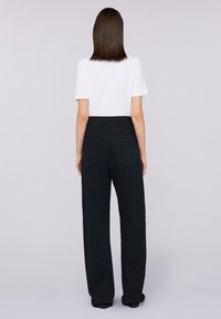 Camiseta blanca de manga corta combinada con pantalones de mezclilla oscuros de tiro alto y perneras anchas, que cuentan con bolsillos traseros con un sutil detalle de costura.