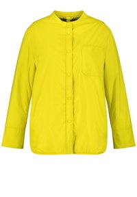Žlutá bunda na knoflíky s kulatým límcem, dlouhými rukávy a kapsou na hrudi. Vyrobena z hladké, lehké tkaniny s matným povrchem.