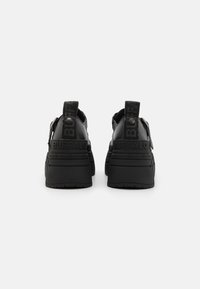 Adidași negri, masivi, cu un superior din piele fină, talpă din cauciuc rezistent și detalii cu logo embosat pe călcâi și curelele gleznei.
