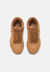 Beżowe zamszowe trampki w niskim fasonie, z gumową podeszwą i płaskimi brązowymi sznurowadłami. Posiadają etykietę na języku w wzór w kratkę oraz branding po bokach.