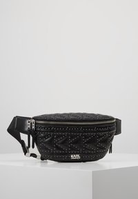 Musta tikattu nahkainen vyölaukku hopeisilla niiteillä, säädettävällä hihnalla ja vetoketjullisella sulkimella. Edessä logolaatta.