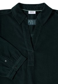 Tummanvihreä korduroy-paita, jossa on kauluskaarro, nappikädensijat ja puolipitkä nappilista. Tunnukset näkyvät kauluksessa ja alaompeleessa.