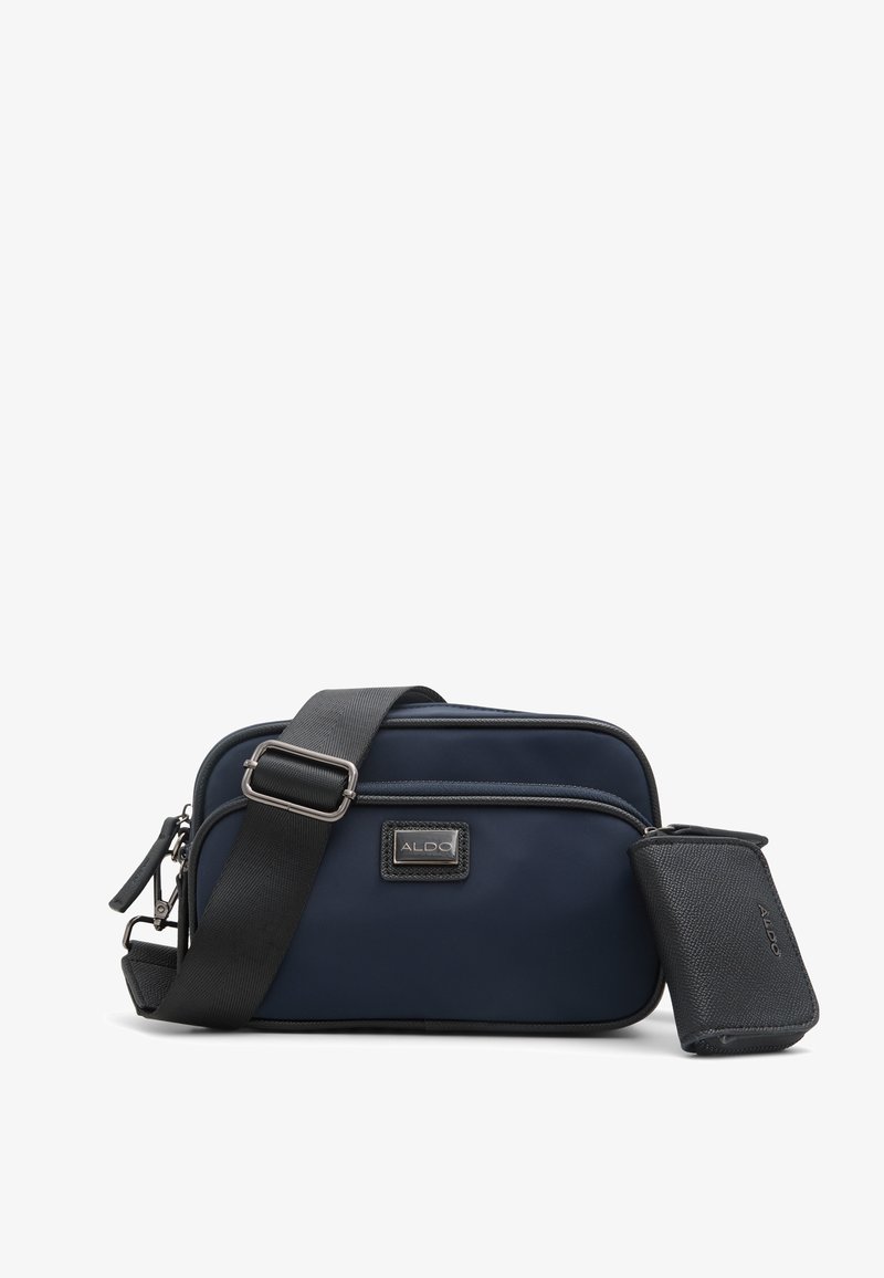 Navy blue crossbody bag with black strap, featuring a smooth texture and zippered compartments; includes a small pouch with a textured finish.