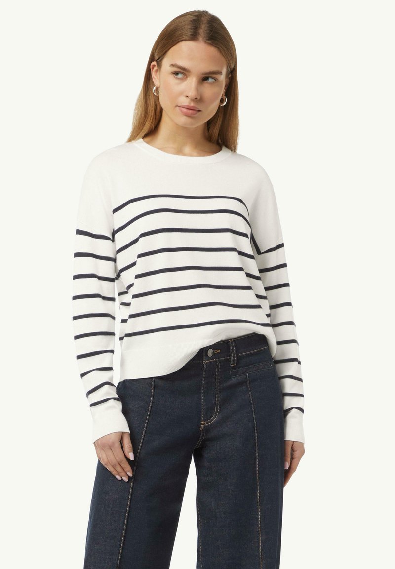 Weißer Strickpullover mit marineblauen horizontalen Streifen, Rundhalsausschnitt und langen Ärmeln, kombiniert mit dunklen Jeans aus Denim mit sichtbaren Nahtdetails.