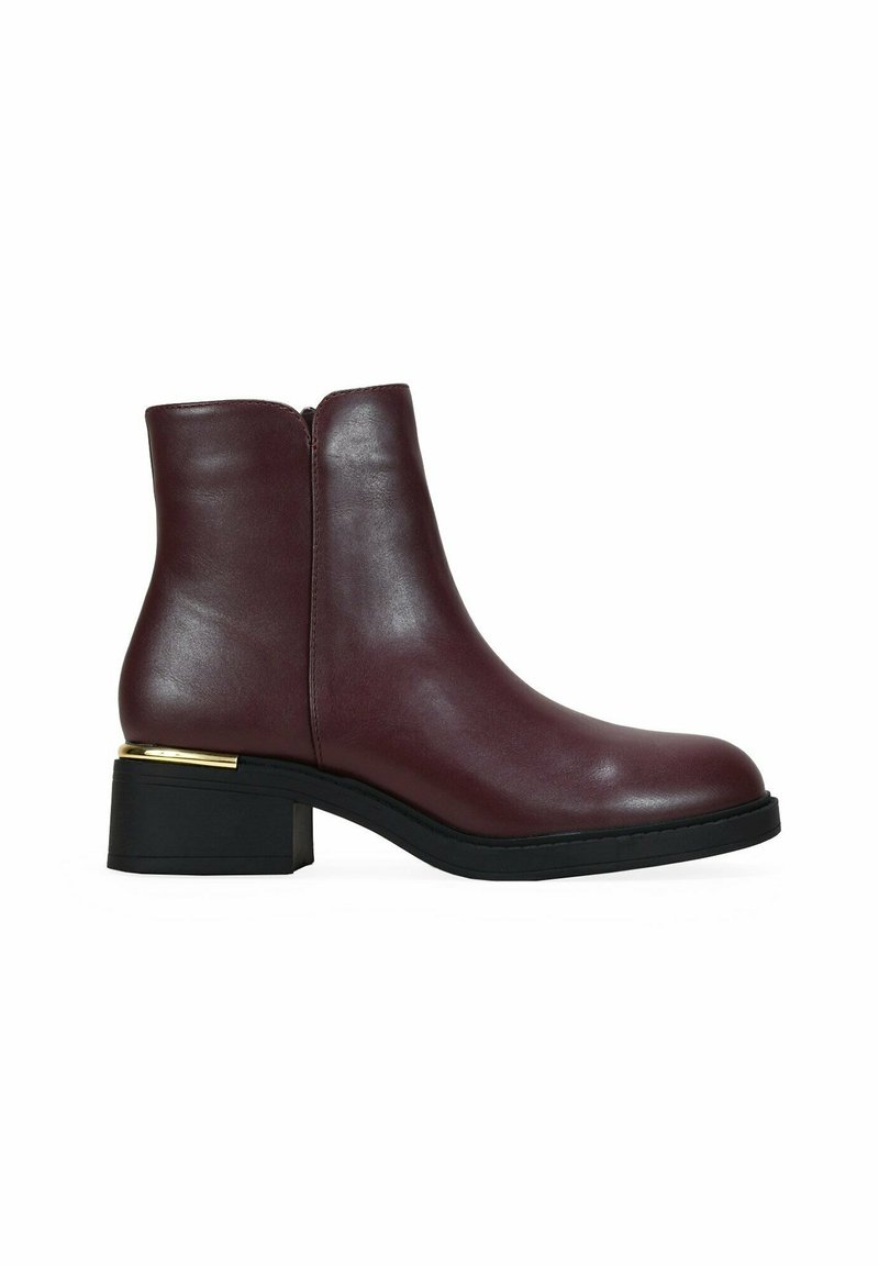 Bottine en cuir bordeaux avec une texture lisse, accent en argent sur le talon et un petit talon carré. Fermeture éclair sur le côté pour un enfilage facile.