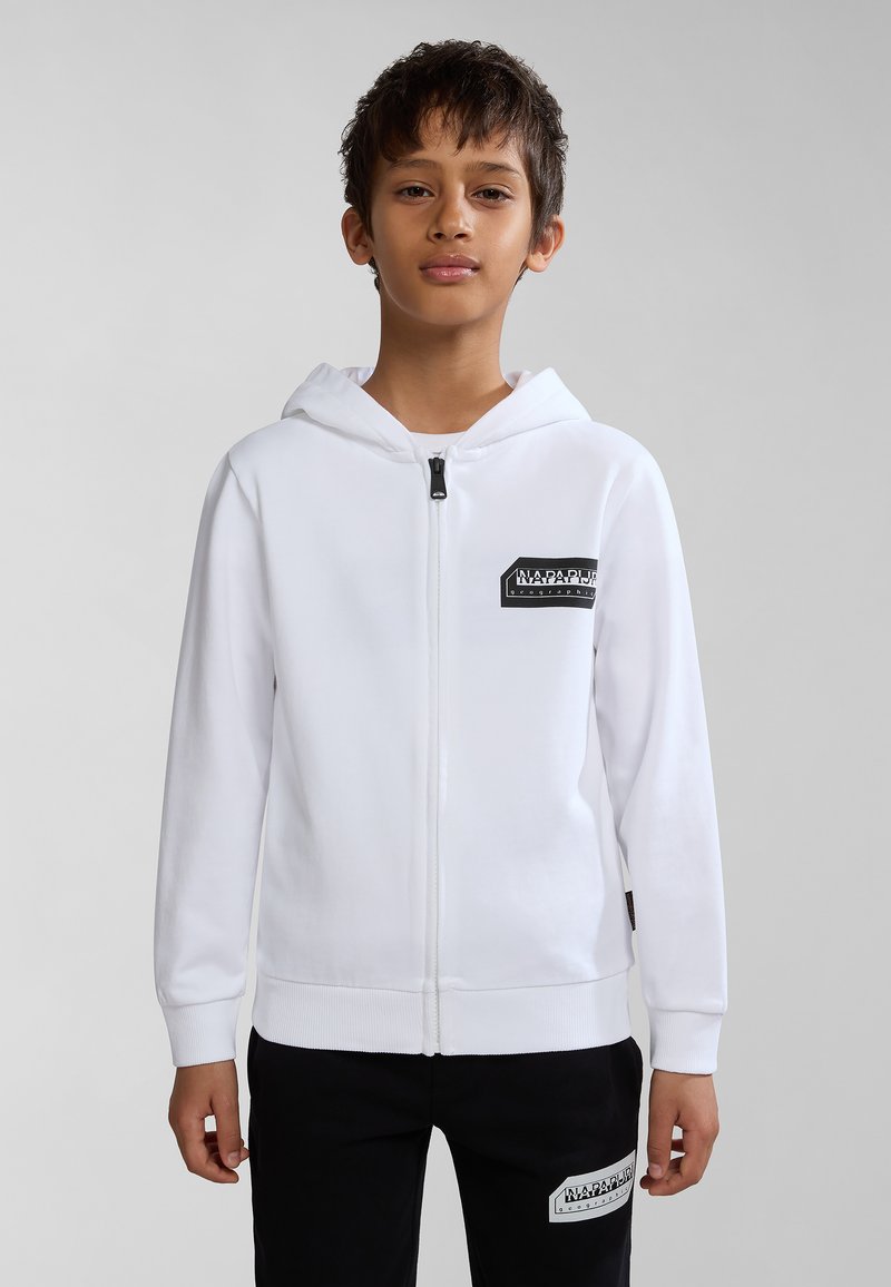 Witte hoodie met rits en een voorzak, voorzien van een zwart logo patch, met een capuchon en geribbelde manchetten, gecombineerd met zwarte broek met een logo.