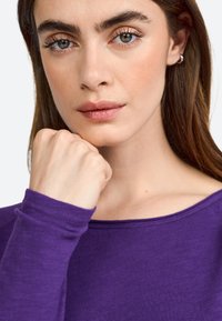 Purple long-sleeve top with a round neckline, worn by a person. Features soft texture and fitted sleeves, with an emphasis on the neckline.