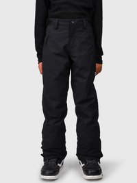 Person som har på seg svarte glidelåsbukser og svarte joggesko med hvite såler, står foran en ensfarget bakgrunn.