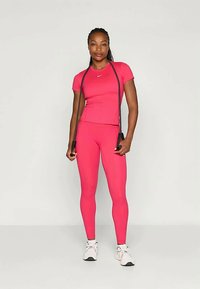 Tettsittende atletisk antrekk i knall rosa med korte ermer, matchende leggings, og et hoppetau i tau. Materialet ser glatt og elastisk ut.