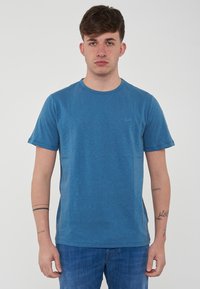 T-shirt di cotone blu con collo rotondo, maniche corte e un logo discreto sul petto. Tessuto morbido, vestibilità casual e design semplice.
