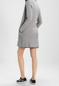 Szary sweterkowy swetrowy fason z długimi rękawami, bocznymi kieszeniami i krawędzią sięgającą powyżej kolan. Noszony z czarnymi tenisówkami.