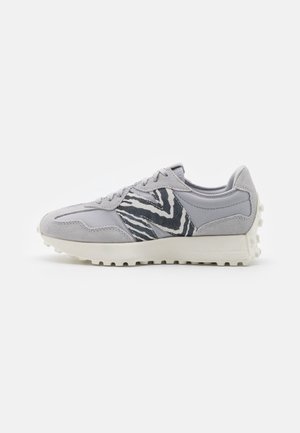 Zapatilla deportiva gris con un detalle de tela con patrón de cebra, detalles en ante y una suela de goma texturizada para mejor agarre.