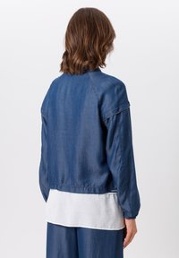 Donkerblauwe denimjas met lange mouwen, elastische manchetten en een cropped ontwerp. Beschikt over een gelaagde witte stof eronder.