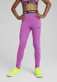 Lilla leggings med sort PUMA-logo på kanten og sømmene; parret med lysegule træningssko. Glat, strækbart stofdesign.