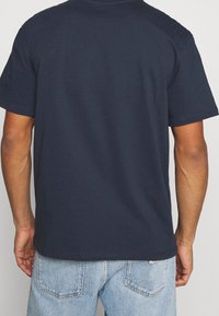 Camiseta de algodón azul marino con mangas cortas, corte relajado y escote redondo. Costuras visibles a lo largo del dobladillo y los hombros.