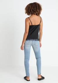 Camisole en satin noir avec bretelles réglables et dentelle, associé à un jean skinny bleu clair. Sandales plates noires à enfiler. Vue arrière.