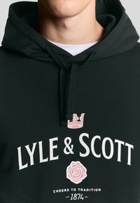 Felpa nera con un design frontale che presenta "LYLE & SCOTT" in testo bianco, una corona rosa e un emblema di rosa rosa. Il testo include "CHEERS TO TRADITION 1874."