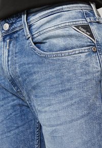 Helle blaue Jeans mit klassischer Passform, ausgestattet mit einer Vordertasche, schwachem Used-Look und einem dunklen Label auf der Gesäßtasche.