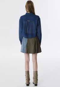 Denim cropped jack met een blauw gestreept textuur, gecombineerd met een geplooide groene en denim rok. Tan kniehoge laarzen met decoratieve knopen.