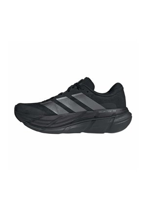 Zapatilla de correr Adidas negra con suela gruesa y tres rayas reflectantes, etiquetada como Dreamstrike Pro en la entresuela.