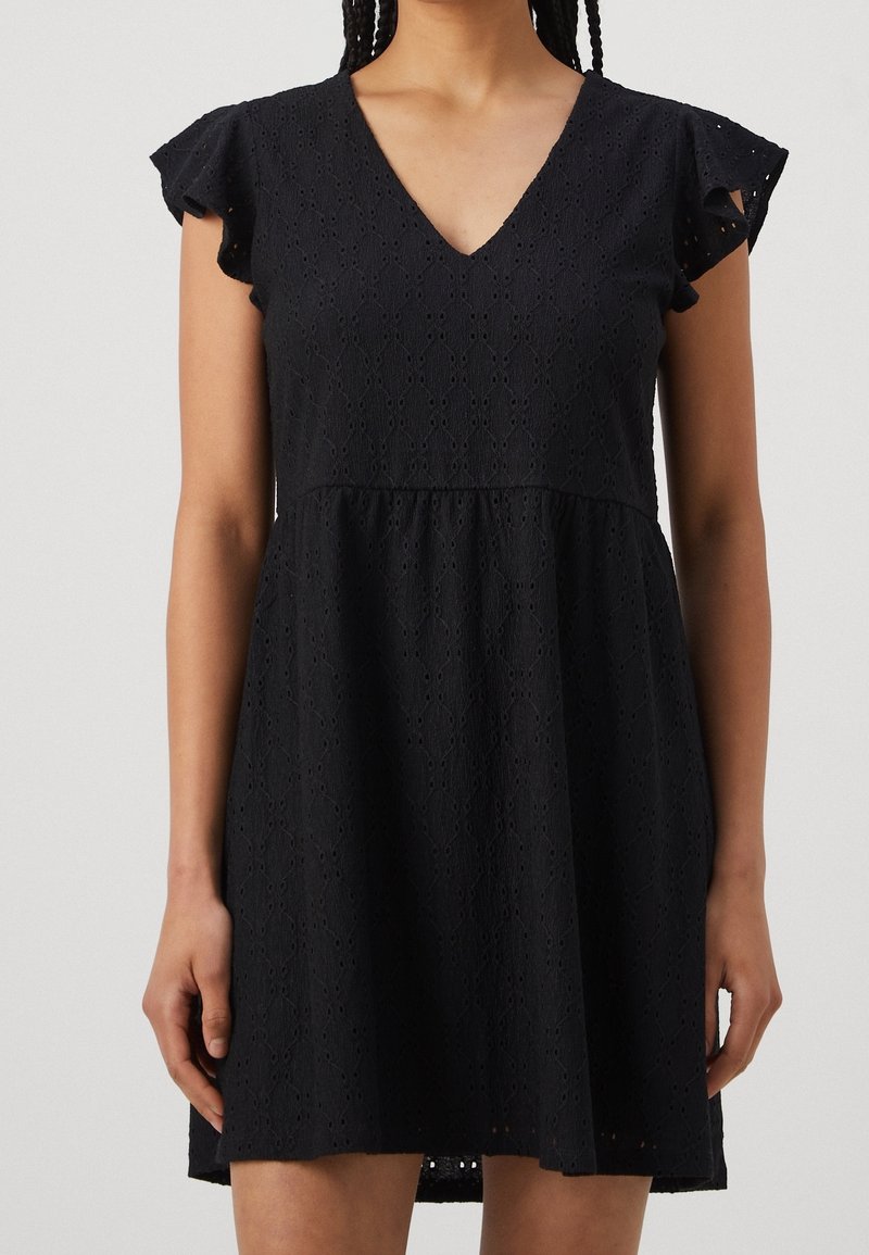 Robe noire avec un décolleté en V, des manches courtes à volants et un tissu texturé avec des motifs à œillets. Corsage évasé avec une jupe froncée.