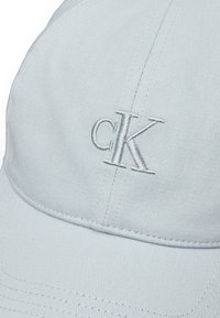 Căciulă de baseball de culoare albastru deschis, dintr-un material texturat, având un logo brodat "cK" pe partea din față. Include accente cusute pentru durabilitate.