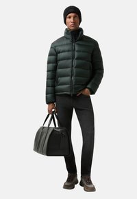 Dark green puffer jacket with horizontal stitching, black beanie, black leather bag, gray jeans, and brown sneakers with accents.