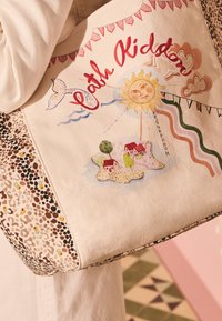 Liela soma ar uzrakstu "Cloth Kids", sauli ar seju, mazu salu ar mājām un koku, viļņainām līnijām un leopardu raksta sānu paneļiem.