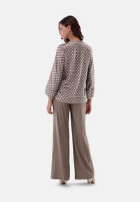 Blusa a pois marroni con maniche lunghe, abbinata a pantaloni beige a gamba larga. Tessuto morbido con una vestibilità rilassata e una sottile lucentezza.
