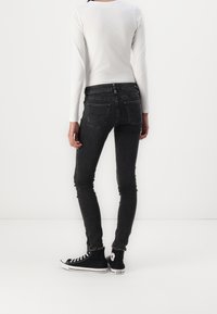 Jeans negros ajustados con un acabado desgastado y diseño de cinco bolsillos, combinados con una camiseta blanca de manga larga y deportivas negras de caña alta.