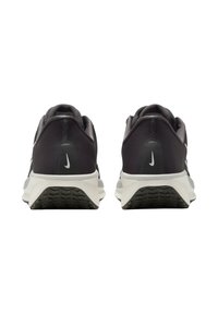 Par de zapatillas de running Nike en blanco y negro vistas desde atrás, con los logotipos de Nike visibles en los talones y suelas negras con patrón.