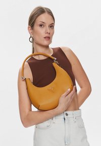 Borsa gialla realizzata in materiale testurizzato; forma curva con un manico corto; presenta un dettaglio del logo vicino alla parte superiore; indossata sottobraccio.