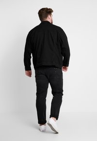 Black denim jacket with a relaxed fit, featuring long sleeves and a button closure. Paired with black jeans and white sneakers.