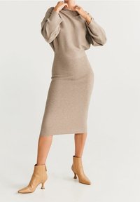 Robe en tricot beige avec une silhouette ajustée, un col rond et des manches bouffantes, associée à des bottines beiges à bout pointu.