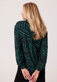 Czarna bluzka w zielono-niebieskie paski zebra, z długimi rękawami i mankietami na guziki. Tył ozdobiony jest miękkim materiałem, co zapewnia luźny krój.