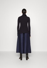 Haut à col roulé côtelé sombre associé à une jupe maxi en satin bleu marine fluide et des bottes noires à talons, vu de dos.