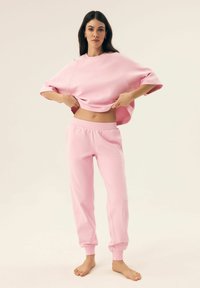 Różowy skrócony sweter z szerokimi rękawami i dopasowanymi spodniami dresowymi. Wykonany z miękkiego materiału, z prostym wzorem i luźnym krojem.