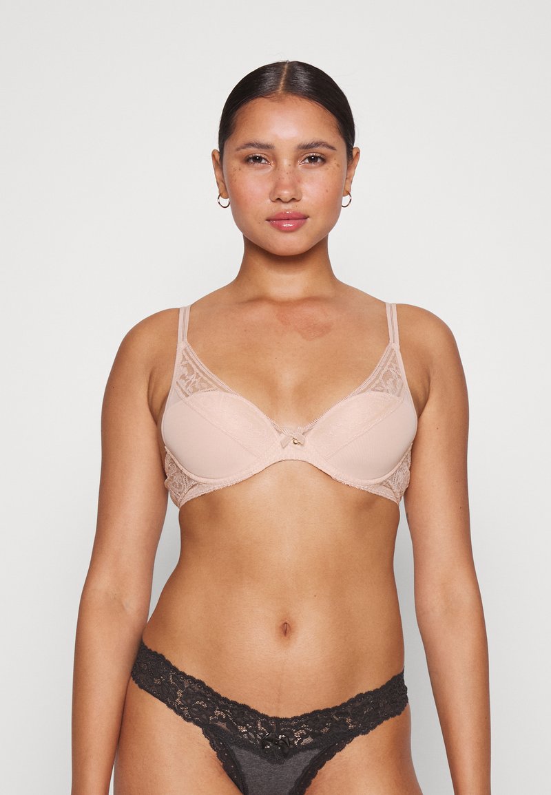 Sutiã de renda rosa claro com copas suaves e alças ajustáveis; apresenta um pequeno detalhe de laço no centro. Combinado com uma tanga de renda preta.