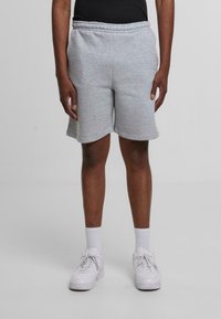 Person iført lysegrå knælange shorts, hvide sokker og hvide sneakers, stående foran en ensfarvet lys baggrund.