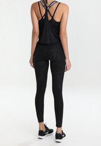 Top in tessuto tecnico nero con design a schienale sportivo, abbinato a leggings neri con stampa leopardata a rilievo. Indossato con scarpe da ginnastica nere.
