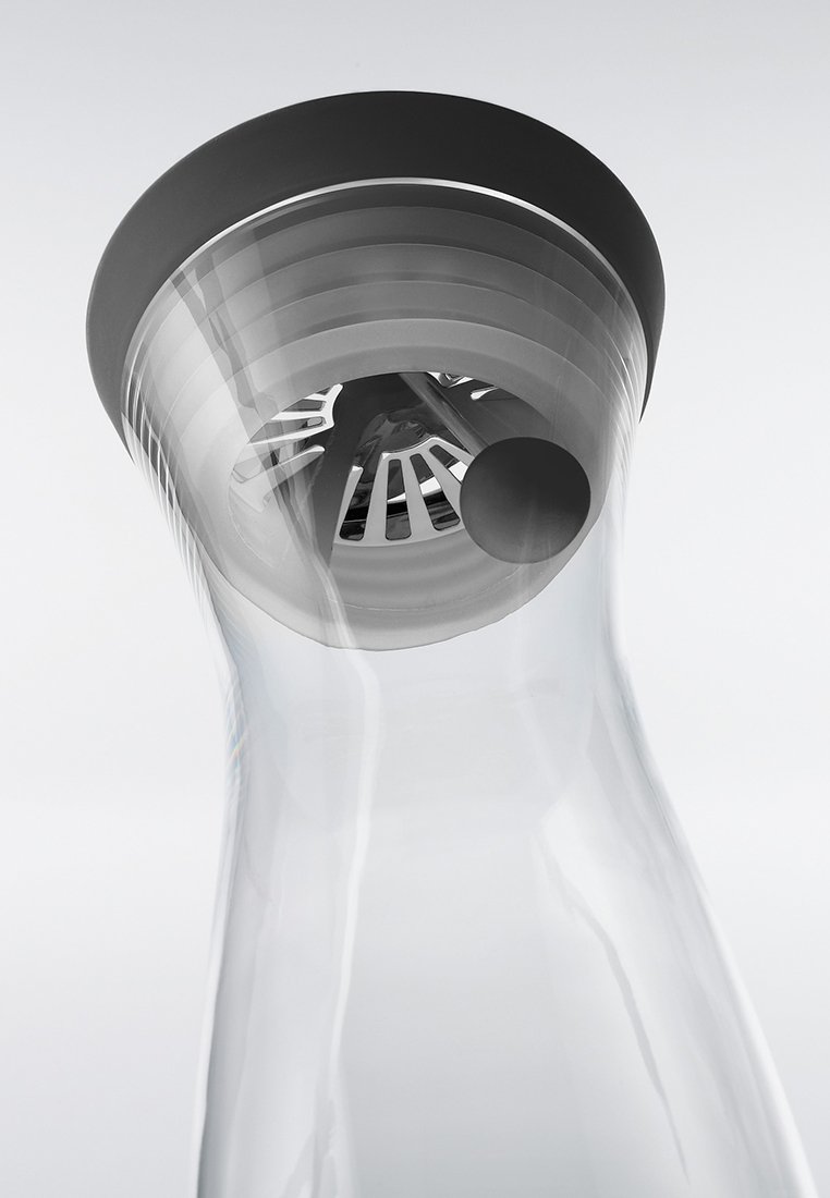 Carafe à eau en verre clair avec un couvercle en élastique noir, présentant un bec circulaire et un design de filtre fendu pour verser des boissons.