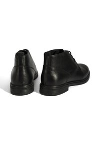 Bottines en cuir noir avec une finition texturée, bout rond et laçage. Caractéristiques d'une semelle lisse et d'un talon arrondi.